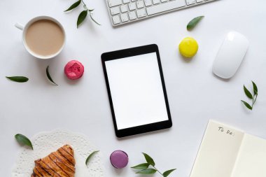 Tablet, klavye, bir fincan kahve, kruvasan, badem kurabiyesi ve çiçekli maket.