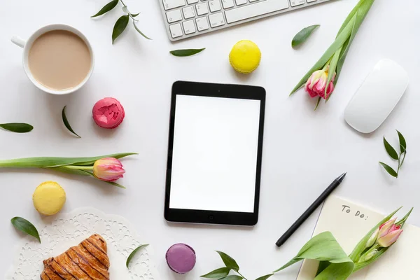 Tablet, klavye, bir fincan kahve, kruvasan, badem kurabiyesi ve çiçekli maket.