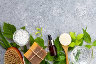 Bitkisel malzemeli doğal kozmetikler: sabun, aljinat maskesi, serum, deniz tuzu, gri arka planda aloe vera jeli, üst görünüm