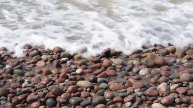 Deniz sahilinde çakıl taşları, köpüklü dalgalar.
