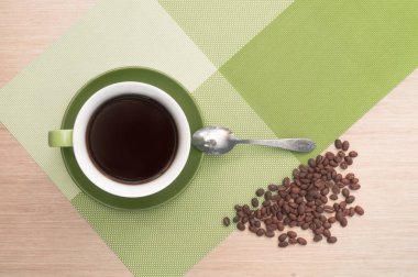 Yeşil fincan kahve tablo arka planı ve masa örtüsü, fasulye ve kaşık.