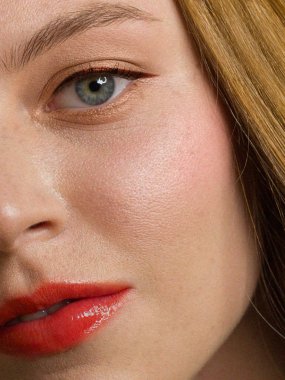 Yarı yüzü kızıl saçlı, çilli ve uzun saçlı. Temiz cilt, açık makyaj, seksi görünüş. Dudaklarda kırmızı ruj, gözlerde kalem, yanaklarda hafif kızarıklık. Spa ve kozmetoloji