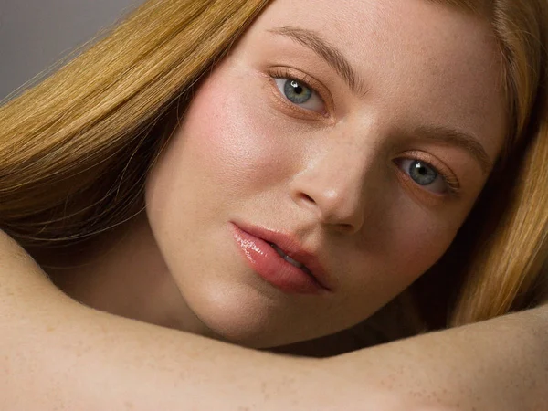 Freckles Woman portrait. Close-up. A beautiful gray-eyed girl with freckles is looking at the camera, on white background. Skin care. The beauty of red straight hair. Beautiful nude makeup. Pink lips