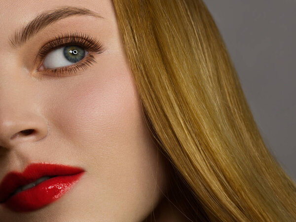 Half of the face of a beautiful redhead with freckles and long red hair. Clean skin, light makeup, sexy look. Red lipstick on the lips and extremely long eyelashes on the eyes. Spa and cosmetology
