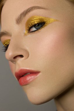 Güzel, yakın plan seksi genç bayan akşamı koyu renk kirpikleri, kızıl kirpikleri, istiflenmiş saçları, altın teni, kamera makyözünün kozmetik güzellik salonu kaplıcasına bakıyor. Altın mücevher