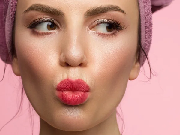 Close-up of a female portrait with a towel on her head and evening make-up. Arrows in the eyes and extremely long eyelashes. Makes a kiss on camera. Clean skin and pink lips. Thick even eyebrows — 스톡 사진