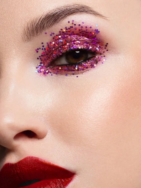 Nahaufnahme der Schönheit des Gesichts einer halben Frau mit kreativem modischem Make-up aus Funkeln. schwarzer Eyeliner und lange Wimpern schmücken Augen und Lippenstift und leuchten rot glitzernd. Gepflegte Haut nach dem Wellness — Stockfoto