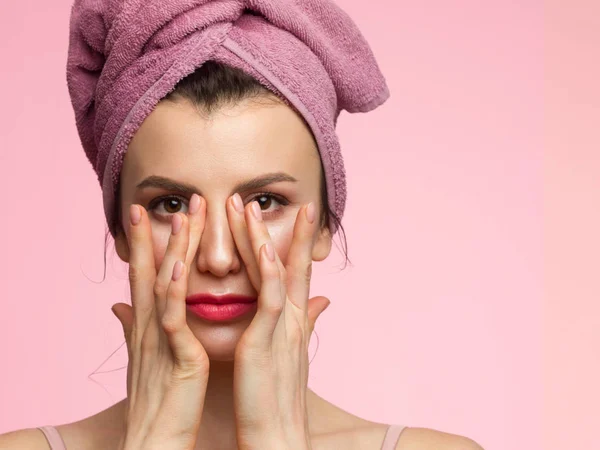 Beautiful woman with clean perfect skin. Portrait of beauty model with natural nude make up and touching her face. Spa and wellness. Close up pink background, copy space. Pink lipgloss, thick eyebrow