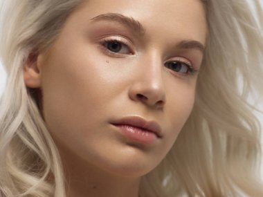 Düz saçlı bir kadının yakın plan portresi. Sevimli genç sarışın kız. Doğal ruj, şeffaf temiz ten. Spa salonunda ya da kozmetolojide cilt bakımı doğal kozmetik ürünleri.