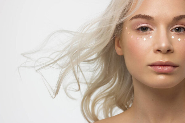 Крупный план портрета женщины с блестящей чистой кожей и вьющимися светлыми волосами. Горячие камни звезды на глазах, голый макияж и натуральная помада. мягкий уход, полные губы, длинные ресницы и толстые брови
