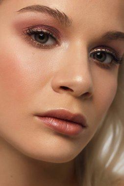 Siyah dumanlı göz makyajı ve doğal dolgun dudakları olan güzel bir kadının temiz yüzünün yakın plan portresi. Temiz ciltli, temiz yüzlü, uzun kıvırcık saçlı seksi bir manken. göz kamaştırıcı görüntü