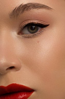 Yaratıcı moda gecesi makyajlı, yarı kadın yüzünün yakın plan güzelliği. Gözlerde siyah oklar ve son derece uzun kirpiklerde, tam kırmızı dudak mat kırmızı dudak rengi. Kaplıcadan sonra iyi bakımlı cilt