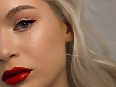 Yaratıcı moda gecesi makyajlı, yarı kadın yüzünün yakın plan güzelliği. Gözlerde siyah oklar ve son derece uzun kirpiklerde, tam kırmızı dudak mat kırmızı dudak rengi. Kaplıcadan sonra iyi bakımlı cilt