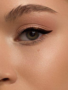Klasik göz kalemi makyajlı güzel bir makro kadın gözü. Mükemmel kaşlar, kahverengi göz farı ve uzun kirpikleri. Makyaj malzemeleri ve makyaj malzemeleri. Moda gemisi bakışlarının yakın çekim makro çekimi.
