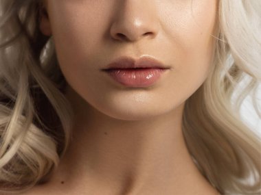 Cinsel dolgun dudaklar. Dudak parlatıcısı ve kadın derisi. Ağız kapalı. Dudaklarda ve kozmetolojide artış. Pembe dudaklar ve uzun boyun. Yumuşak saf ten ve dalgalı sarı saçlar..