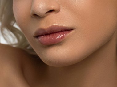 Cinsel dolgun dudaklar. Dudak parlatıcısı ve kadın derisi. Ağız kapalı. Dudaklarda ve kozmetolojide artış. Pembe dudaklar ve uzun boyun. Yumuşak saf ten ve dalgalı sarı saçlar..