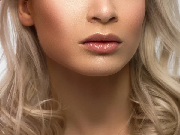 Close-up of woman\'s lips with fashion natural beige lipstick makeup. Macro sexy pale lipgloss make-up . Gentle pure skin and wavy blonde hair. Cosmetology, Spa, increase in lips. Face powder