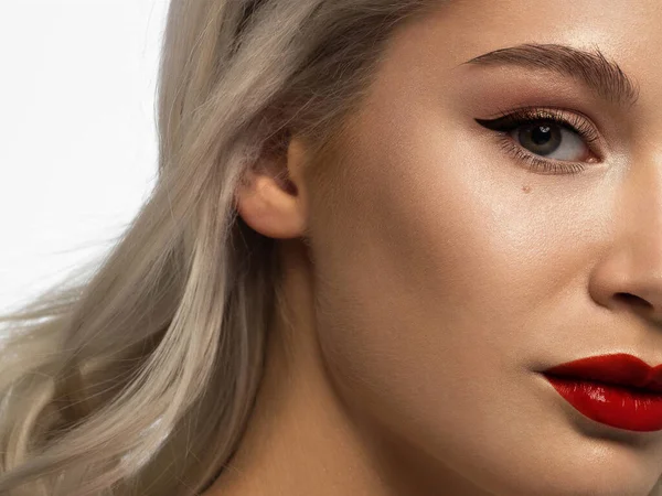 Close-up beauty of half female face with creative fashion evening make-up. Black arrows on the eyes and extremely long eyelashes, on full red lips matte scarlet lip color. Well-groomed skin after spa