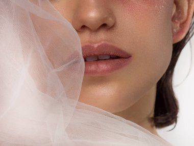 Güzel ciltli ve çıplak makyajlı kadın dudaklarının makro fotoğrafı. Dolgun dudaklarda şeffaf bir parlatıcı ve beyaz çiçekler. Moda fotoğrafçılığı. Kozmetik ve kaplıca. Baharın tazeliği