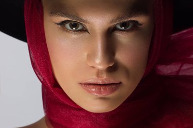 Şapkalı, siyah göz kalemi ve kırmızı atkısı olan güzel bir kadın. Temiz ve parlak ten, doğal dudak parlatıcısı, kalın kaşlar ve uzun kirpikler. Vintage fotoğrafçılık, kozmetoloji ve makyaj.