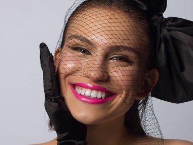 Düğüm ve peçeli, siyah göz kalemi ve pembe rujlu, şık yarı güzel bir kadın. Temiz ve parlak cilt, doğal dudak parlatıcısı, kalın kaşlar ve uzun kirpikleri. Kozmetik ve makyaj.