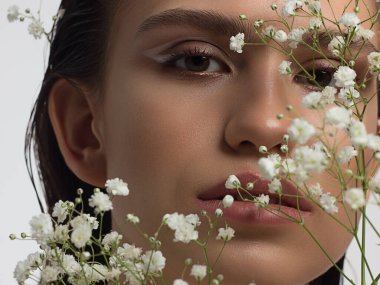 Güzel derisi, çıplak makyajı, göz kalemi, uzun kirpikleri, kabarık doğal dudakları ve beyaz çiçekleri olan bir yüz portresi. Moda fotoğrafçılığı. Kozmetik ve kaplıca. Baharın tazeliği