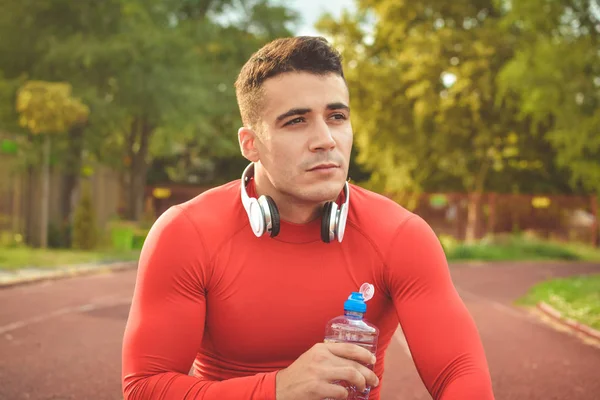Athletic sport man drinking water from a bottle. Cold drink after outdoor fitness
