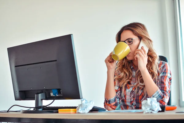 Mujer creativa hablando por teléfono mientras está sentada en el escritorio en la oficina — Foto de Stock