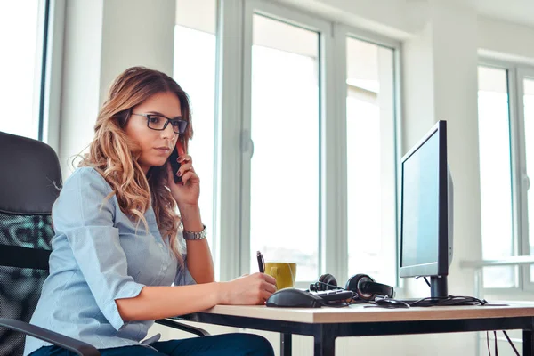 Mujer creativa hablando por teléfono mientras está sentada en el escritorio en la oficina — Foto de Stock