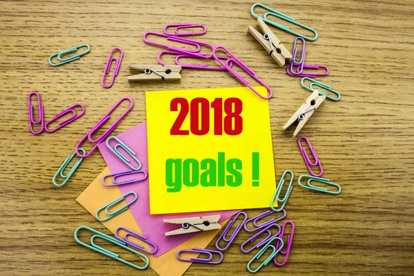 2018 goals on yellow sticky note, on wooden background. New Year resolutions concept.