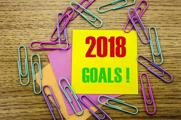 2018 goals on yellow sticky note, on wooden background. New Year resolutions concept.