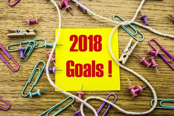 2018 goals on yellow sticky note, on wooden background. New Year resolutions concept.