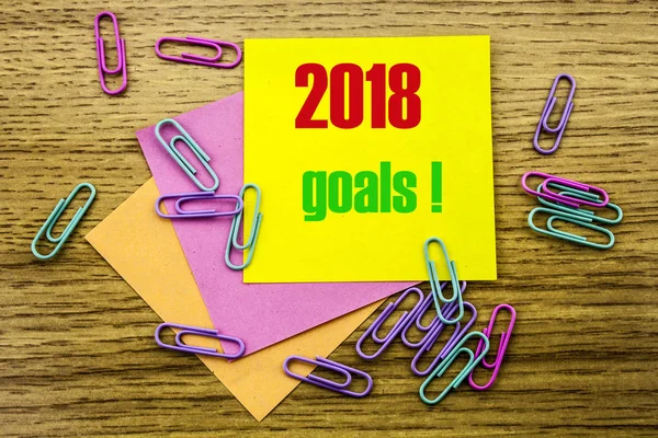 2018 goals on yellow sticky note, on wooden background. New Year resolutions concept.