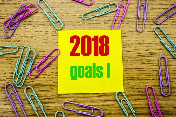 2018 goals on yellow sticky note, on wooden background. New Year resolutions concept.