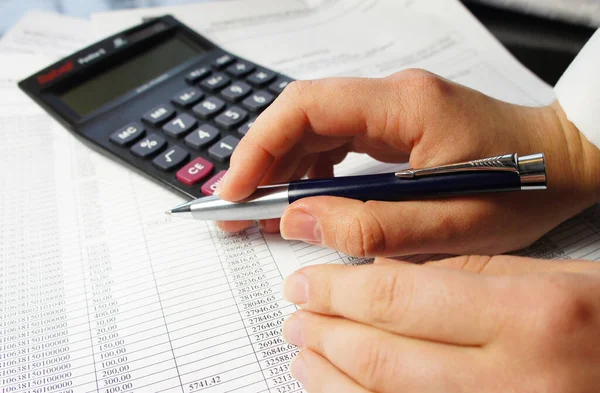 Calculator, pen and accounting document with a lot of numbers and woman hands