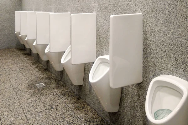 Publiczna toaleta z szarymi ścianami i wieloma białymi pisuarami — Zdjęcie stockowe