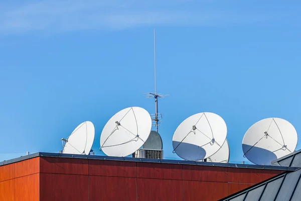 many white parabolic satellite antena dishes on the roof of the house. Wireless television broadcasting recievers