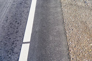 Çakıl taşı şeridi ve beyaz yol kenarı olan asfalt bir yol.