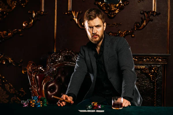 A wealthy mature man smoking cigar and playing poker in a casino. Gambling, playing cards and roulette.