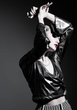 Kendine güvenen, şık kıyafetler giyen ve gri arka planda stüdyoda poz veren bir kadının portresi. Güzellik, makyaj, tarz.