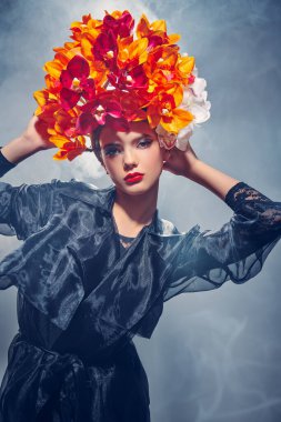 Güzellik, moda çekimi. Kafasında parlak turuncu ve klasik orkidelerden oluşan gri bir arka planda duran güzel bir kadının portresi. Bahar ve yaz güzelliği. Parfüm.