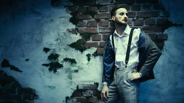 Art, history and fashion. A young man with makeup in the style of the 20s poses in an elegant suit on the background of an old ruined wall.