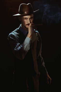 Zarif klasik takım elbiseli yakışıklı bir adamın portresi ve gölgede sigara içen bir şapka. Retro tarzı. Lüks bir yaşam tarzı. Erkek güzelliği, moda.
