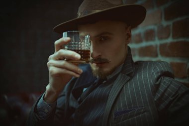 Yakışıklı sarhoş bir adam deri koltukta bir bardak viskiyle rahatça oturuyor. Lüks bir yaşam tarzı. Retro tarzı. Mafya ve suç dünyası. 