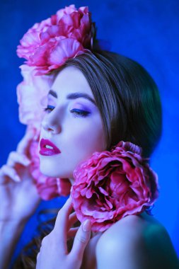 Mavi arka planda şakayık çiçekleri olan güzel bir manken. Moda ve çiçekler. Makyaj ve saç stili. Stüdyo resmi.