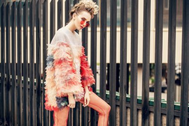 Şehrin varoşlarında poz veren, modern, tüylü, genç bir kadın. Güzellik, sokak modası.