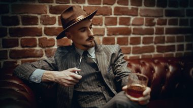 Yakışıklı, kendine güvenen bir adam, zengin bir koltukta, bir pipo ve bir bardak viskiyle rahat bir şekilde oturuyor. Lüks bir yaşam tarzı. Retro tarzı. Mafya ve suç dünyası. 