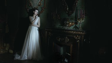 Zarif, beyaz, uzun elbiseli muhteşem bir genç kadının tam boy portresi. Lüks karanlık daireler. Düğün modası.