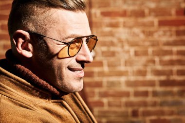 Şık giyinmiş, gözlüklü, saygıdeğer olgun bir adamın portresi tuğla duvar arkasında. İş konsepti. Optik biçimi. 