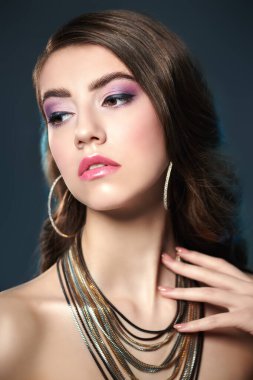 Güzellik, moda ve mücevher. Koyu bir arka planda uzun dalgalı saçlarla poz veren muhteşem bir genç kadının portresi. Mücevher salonu..